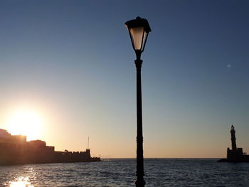 Street light by sea against sky during sunset