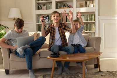Three brother boys playing computer games on a laptop and video games with joysticks
