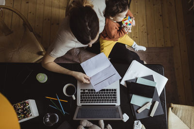 Directly above shot of businesswoman reading document with male toddler working at home