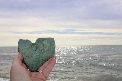 Cropped hand of woman holding sea against sky