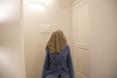 Rear view of woman standing against white wall at home