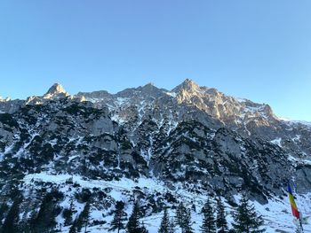 Low angle view of snowcapped mountains against clear blue sky