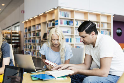 Young university students reading book at desk in library