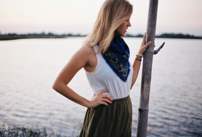 Young woman with hand on hip standing by lake during sunset