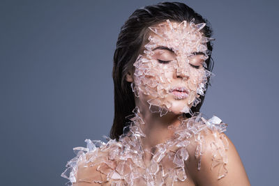 Close-up of woman with broken glass on body against purple background