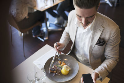 High angle view of businessman using smart phone while eating lunch at restaurant