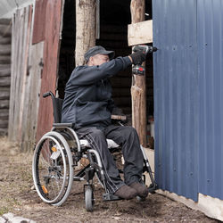 Happy elderly man in casual clothes in a wheelchair is working and building something in his yard.
