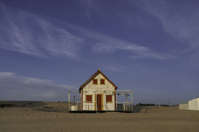 Hut on beach by houses against sky