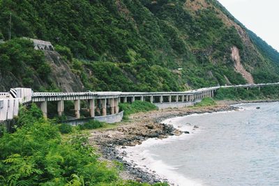 Bridge by sea against green mountain