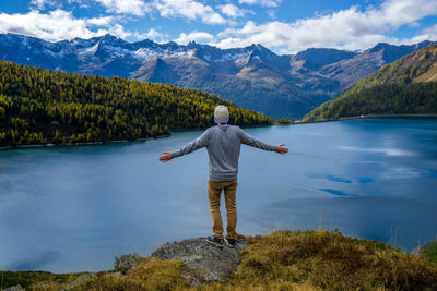 Rear view of man standing by lake against mountain