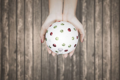 Close-up of cropped hand holding christmas bauble over wooden planks