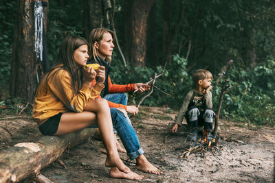 A young mother with her children is sitting by the campfire during a joint holiday