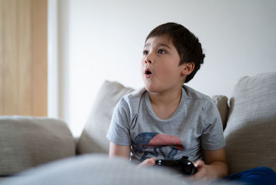 Boy playing video game while sitting on sofa at home
