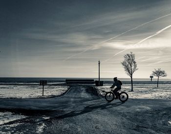 Man on bicycle by sea against sky