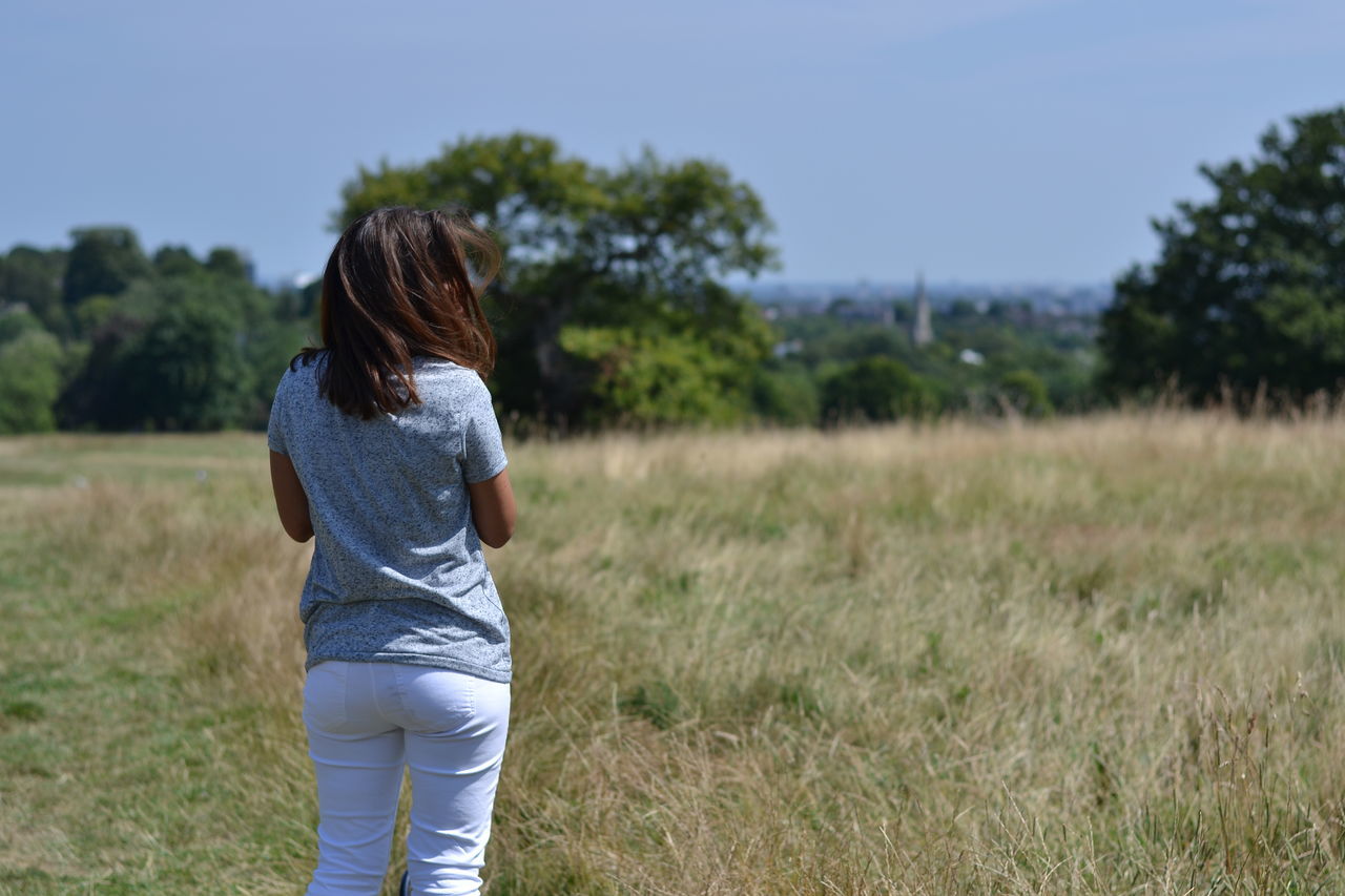 grass, field, lifestyles, leisure activity, rear view, casual clothing, grassy, standing, landscape, three quarter length, tree, focus on foreground, nature, tranquility, green color, person, men, side view