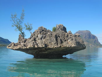 Rock formation in sea against clear blue sky