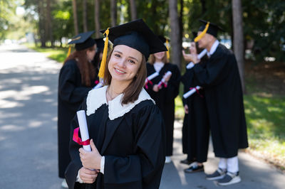 Portrait of woman wearing graduation gown standing in park