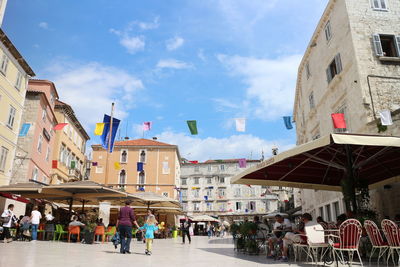 Sidewalk cafe amidst buildings against sky on sunny day