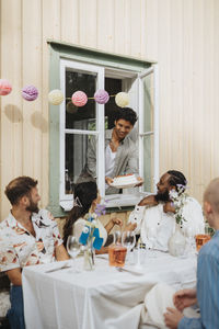 Smiling man giving cake to friends sitting at table during dinner party