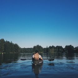 Rear view of man kayaking in lake against clear sky