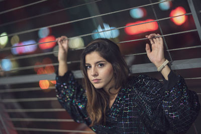 Portrait of young woman standing against railing at night