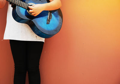 Midsection of girl playing guitar against orange wall