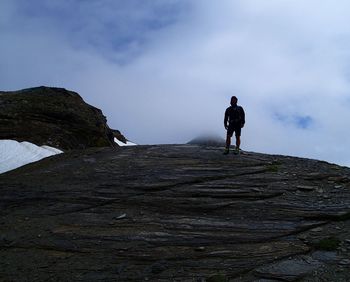 Rear view of man standing on rock against sky