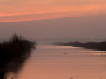 Scenic view of lake against dramatic sky during sunset