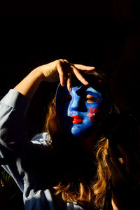 Portrait of young woman wearing mask against black background