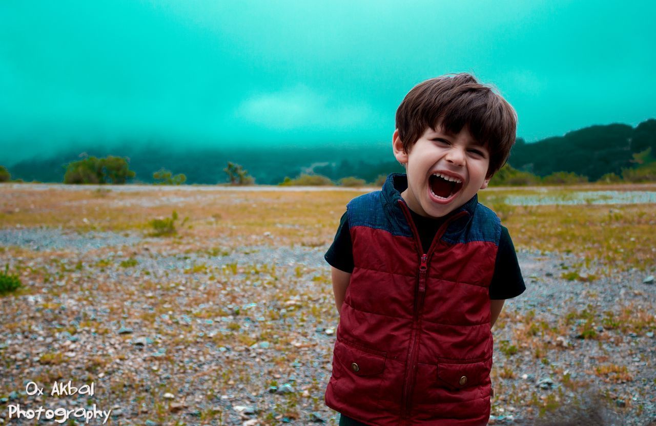 BOY STANDING IN GRASS AGAINST TREES