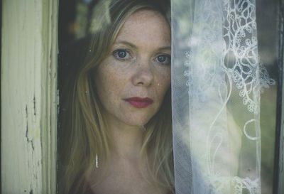 Close-up portrait of young woman seen through window