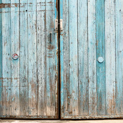 Fragment of very old wooden door with blue cracked paint, parallel boards, full frame