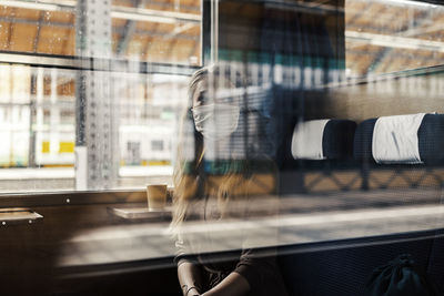 Woman wearing mask sitting in train seen through window