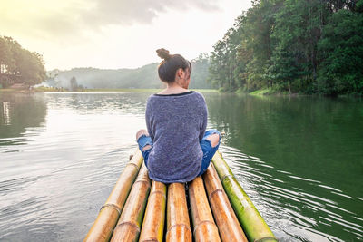 Rear view of man sitting on lake against sky