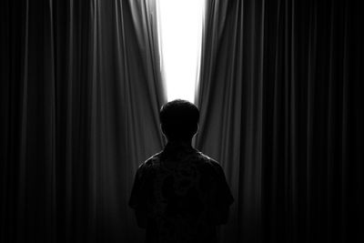 Rear view of man standing against curtain in darkroom