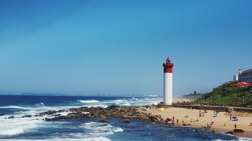 Lighthouse by sea against clear blue sky