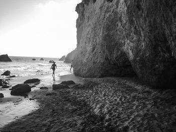 Man walking on cliff by sea against sky