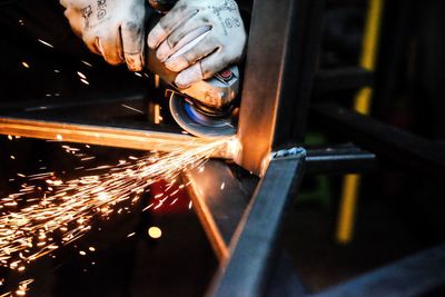 Cropped hands of worker cutting metal with electric saw in workshop