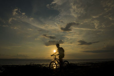 Man riding bicycle on beach against sky during sunset