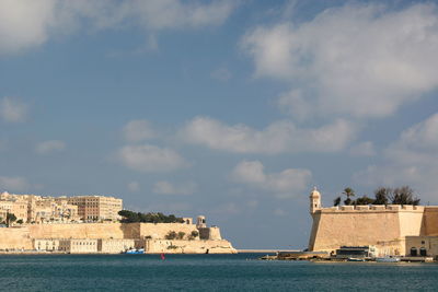 Buildings at waterfront against cloudy sky