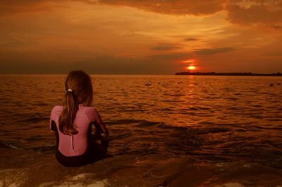 Girl sitting at beach against sky during sunset