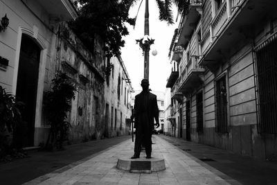 Rear view of man walking on street amidst buildings