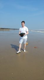 Full length of boy holding rock while walking on shore at beach against sky