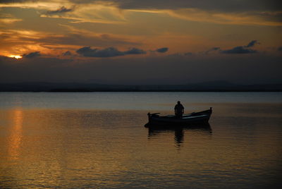 Silhouette man on boat in lake against sky during sunset