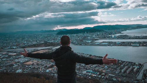 Rear view of man looking down at cityscape against sky