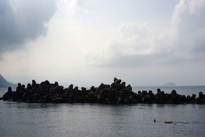 Group of people on rocks by sea against sky