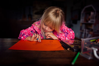 Little blond haired girl drawing a picture at a table on a sunny day