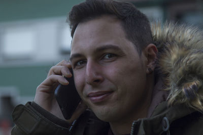 Close-up portrait of smiling young man talking on phone outdoors