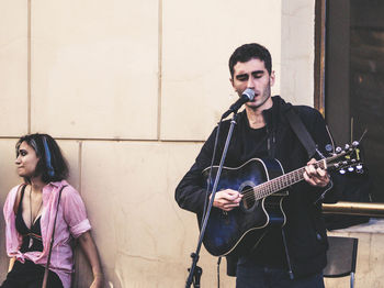 Young man playing guitar against wall