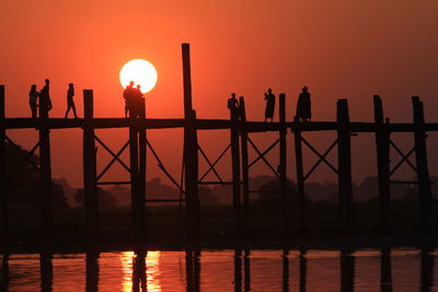 Silhouette people on u bein bridge over river during sunset